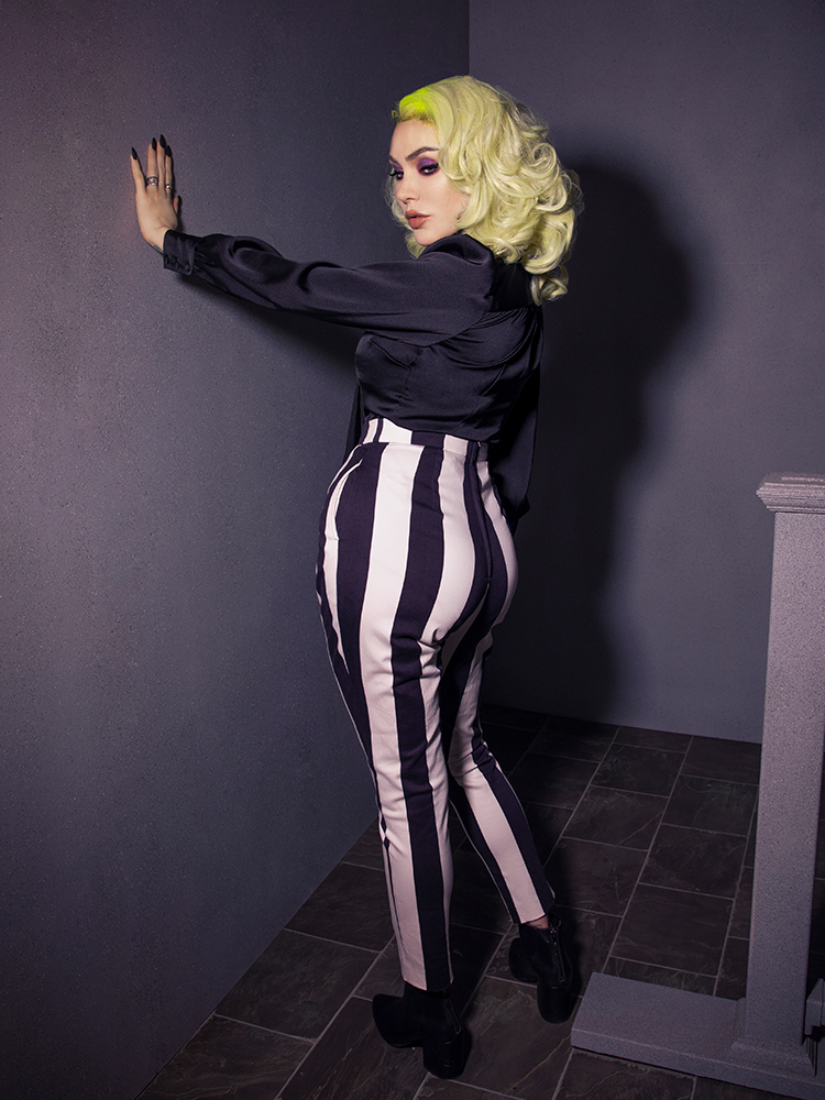 Full length shot of Micheline Pitt wearing the Bowie Blouse w/Matching Tie in Black Charmeuse tucked into black and white striped pants. 