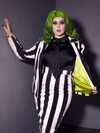 Female model holding open a black and white striped jacket to give a glimpse of the lime green jacket lining. Also featured, the Bowie Blouse w/Matching Tie in Black Charmeuse.
