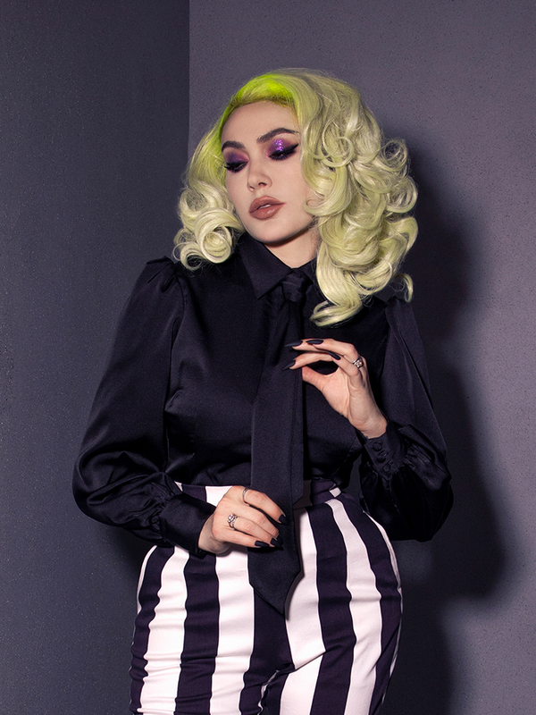 Close up of Micheline Pitt modeling the Bowie Blouse w/Matching Tie in Black Charmeuse tucked into black and white striped pants. 