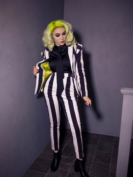 Full length shot of Micheline Pitt wearing a black and white striped jacket and pant combo with the Bowie Blouse w/Matching Tie in Black Charmeuse on underneath. 