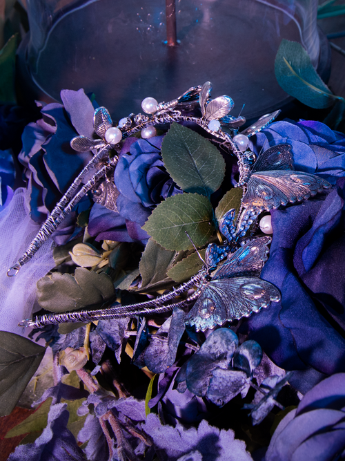 A close-up of the Tim Burton's CORPSE BRIDE™ Emily Butterfly Headband sitting on a bed of roses and silk blankets.