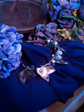 The Tim Burton's CORPSE BRIDE™ Emily Butterfly Headband sitting on a sheet of blue velvet fabric and among flowers.