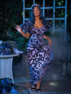Vanessa struts towards the camera while holding up the skirt section of  Tim Burton's CORPSE BRIDE™ Butterfly Maxi Dress in Dusk Blue. 