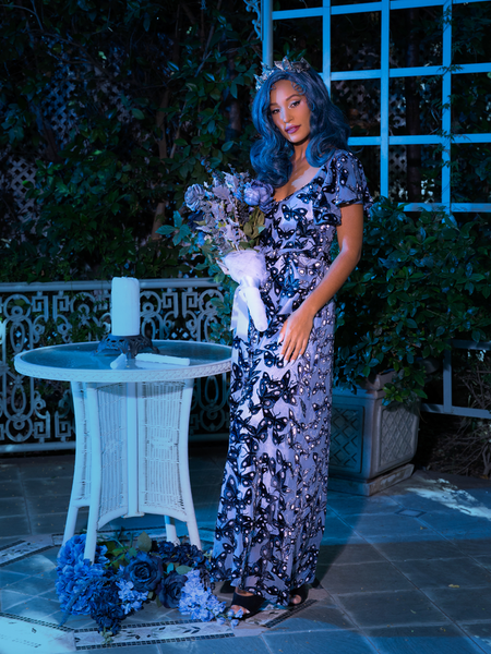 Tim Burton's CORPSE BRIDE™ Butterfly Maxi Dress in Dusk Blue being worn by model  standing in a dimly lit outdoor area. 