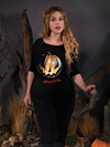 Linda wearing the Sleepy Hollow™ Carved Pumpkin 3/4 Sleeve Tee while resting her hand on the branch of a dead tree while standing in a spooky forest.
