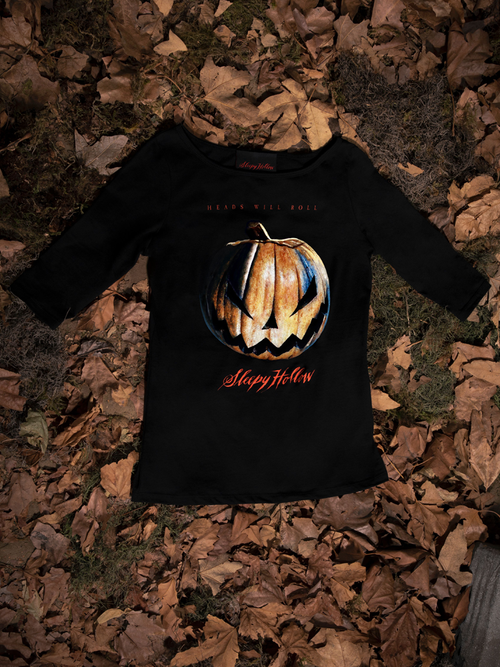 The Sleepy Hollow™ Carved Pumpkin 3/4 Sleeve Tee laying on a bed of dead leaves. 