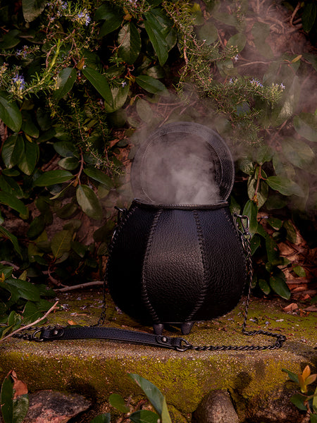 La Femme en Noir's gothic-inspired Cottage Witch Cauldron Crossbody Bag looks stunning against the lush greenery of the garden setting.