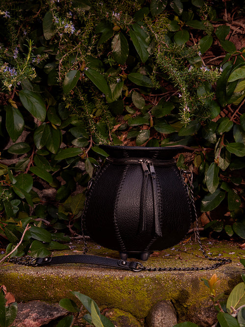 The garden setting is the perfect backdrop for La Femme en Noir's Cottage Witch Cauldron Crossbody Bag, which exudes gothic glamour.