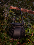 La Femme en Noir's Cottage Witch Cauldron Crossbody Bag, captured in a beautiful garden setting, is the epitome of gothic glamour.