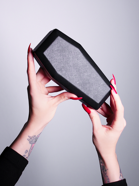 The Vamp Batwing Sunglasses in Black coffin case being held up by fair skinned hands.