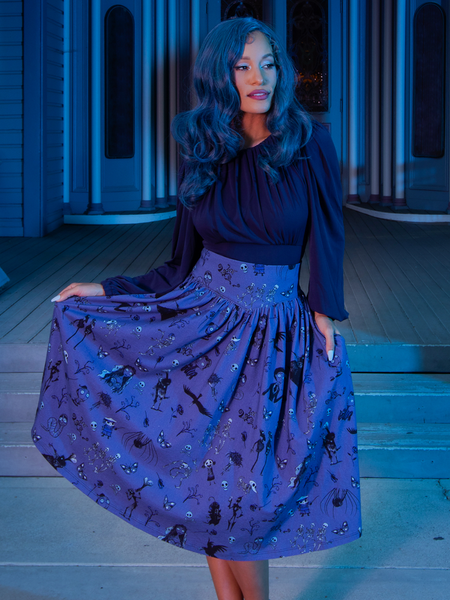 Vanessa wearing the Gothic Tales Skirt in Beyond the Veil Print while standing in front of a moodily lit house.