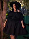 In the mysterious depths of the forest, a fair-skinned brunette beauty radiates charm, donning the Cottage Corset Pinafore in Black, a striking accent piece that complements your gothic dress with perfection.