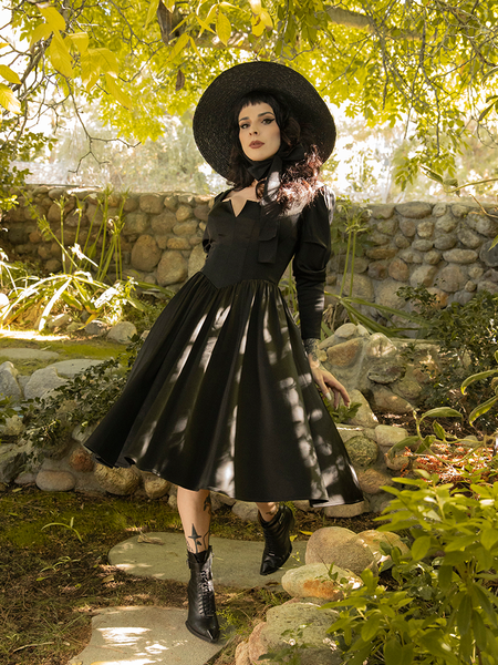 Playfully strutting down a stone pathway, Stephanie wears the Cottage Witch Dress in Japanese Black Satin from goth dress retailer La Femme en Noir.