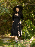 With a subtle smile on her face, Stephanie wears the Cottage Witch Dress in Japanese Black Satin from goth dress retailer La Femme en Noir.