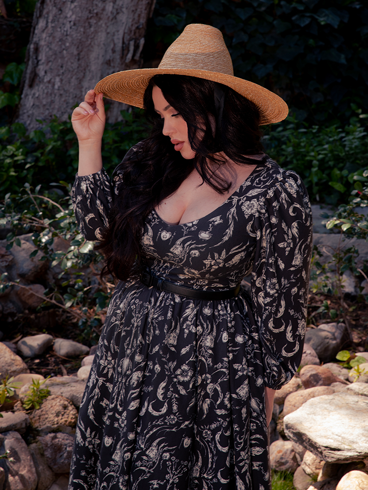 Lost in the Gothic wilderness, an alluring brunette muse emerges, adorned in the hauntingly beautiful Dark Forest Dress featuring the mesmerizing Cottage Witch Toile Print, a masterpiece designed by the renowned La Femme en Noir.