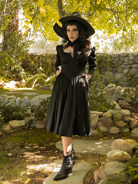 Stephanie with her hands in the pockets of her Cottage Witch Dress in Japanese Black Satin from La Femme en Noir.