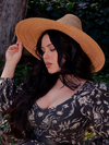 The Cottage Witch Hat in Natural from La Femme en Noir is the perfect accessory that gives the dark haired female model's gothic clothing outfit a touch of elegance and beauty.