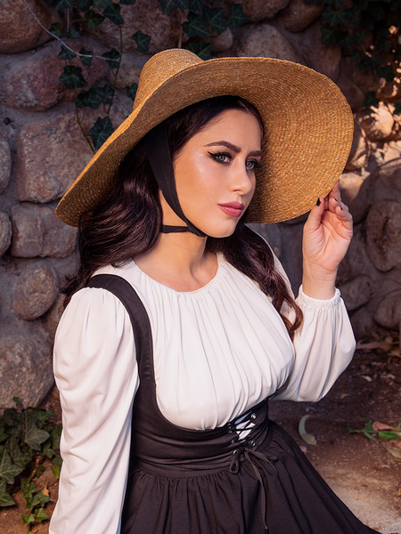 The dark haired female model is an epitome of Gothic beauty in her Cottage Witch Hat in Natural from La Femme en Noir that accentuates her outfit.