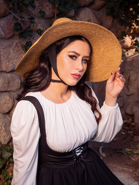 The Cottage Witch Hat in Natural from La Femme en Noir adds a bewitching charm to the dark haired female model's stunning gothic clothing outfit.