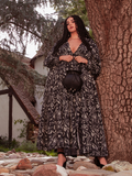 Enthralling in a garden backdrop, the brunette model confidently presents the Belladonna Maxi Dress in Cottage Witch Toile Print from the gothic clothing brand La Femme en Noir.