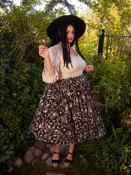 With grace and elegance, the beautiful female model showcases the Gothic Tales Skirt in Cottage Witch Toile Print from the gothic clothing brand La Femme en Noir.