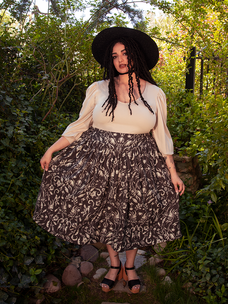 Captivating the audience, the gorgeous female model shows off the Gothic Tales Skirt in Cottage Witch Toile Print from the gothic clothing brand La Femme en Noir.