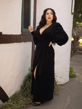 Rachel Sedory standing to the side with one hand on her hip while wearing the Crawford Hostess Wrap Gown in Black from La Femme en Noir.
