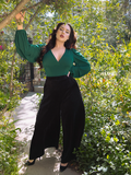 Model Rachel Sedory posing in a flowy green top and the Crawford Palazzo Pants in Black from gothic clothing company La Femme en Noir.