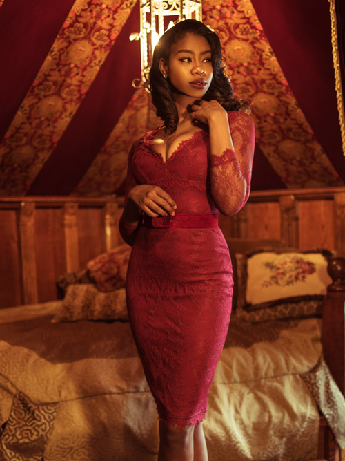 A stylized photo of Chelsea standing in a moody boudoir modeling the La Dentelle dress in crimson.