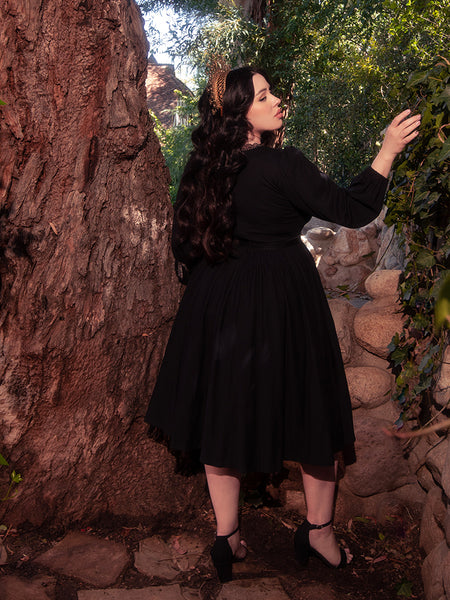 Surrounded by the enchanting allure of a forest, a gorgeous brunette model graces the scene, wearing the elegant Dark Forest Dress in Black, a remarkable creation by the gothic clothing brand, La Femme en Noir.
