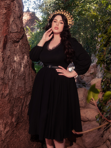 In the midst of a lush forest, a stunning brunette model captivates attention while donning the elegant Dark Forest Dress in Black, an exquisite creation by gothic fashion brand La Femme en Noir.