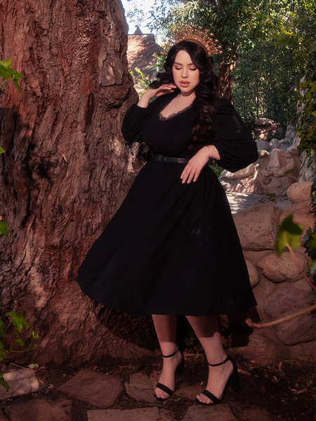 Amidst the verdant expanse of a forest, a mesmerizing brunette model steals the spotlight, dressed in the ethereal Dark Forest Dress in Black, an exquisite piece crafted by the renowned gothic clothing brand, La Femme en Noir.
