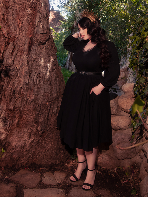 Standing gracefully amidst the enchanting woodland, a breathtaking brunette model radiates beauty, dressed in the mesmerizing Dark Forest Dress in Black, a masterpiece from the gothic clothing label, La Femme en Noir.