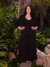 Amidst the tranquility of a wooded forest area, a lovely brunette model exudes grace while wearing the captivating Black Dark Forest Blouse. Unveil the enchantment of La Femme en Noir's collection.