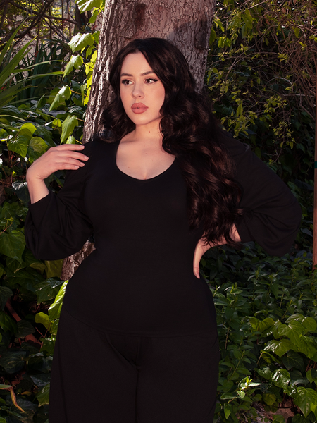 The enchanting brunette model elegantly displays the Black Dark Forest Blouse amidst the lushness of a wooded forest area. Available from the gothic clothing brand La Femme en Noir.