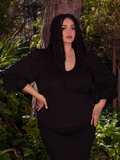 Surrounded by the ethereal charm of a wooded forest area, a brunette model proudly exhibits the Dark Forest Blouse in Black. Embark on a journey into gothic fashion with La Femme en Noir.