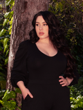 The Dark Forest Blouse in Black finds its perfect setting as a beautiful brunette model poses amidst the tranquility of a wooded forest area. Embrace the allure of La Femme en Noir's gothic fashion.