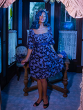Vanessa pulling out the sides of her dress to show off the beautiful butterfly print of Tim Burton's CORPSE BRIDE™ Butterfly Babydoll Dress in Dusk Blue.