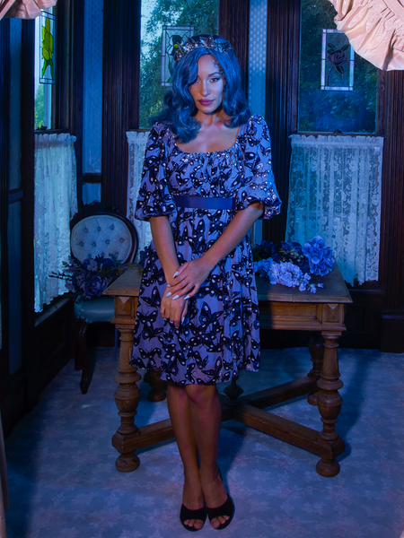 Vanessa standing in the foyer of a dimly lit Victorian house wears Tim Burton's CORPSE BRIDE™ Butterfly Babydoll Dress in Dusk Blue from goth retro clothing company La Femme en Noir.