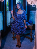 Vanessa poses while lightly pulling out the skirt section of the Tim Burton's CORPSE BRIDE™ Butterfly Babydoll Dress in Dusk Blue from goth dress company La Femme en Noir.