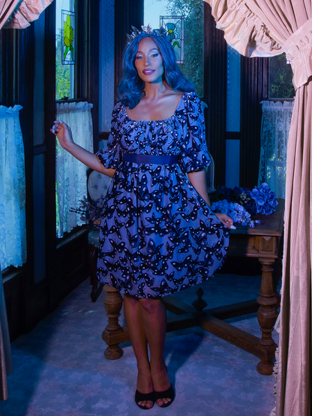 Vanessa poses and smiles gently while looking directly into the camera and wearing the Tim Burton's CORPSE BRIDE™ Butterfly Babydoll Dress in Dusk Blue.