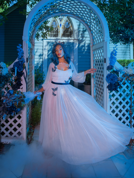 Vanessa poses in Tim Burton's CORPSE BRIDE™ Emily Butterfly Gown in Celestial Blue while standing in a smoky, outdoor garden area.