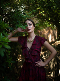 Aliza posing in a lush garden setting while wearing the Mythical Goddess Gown  in Oxblood Gorgon Print.