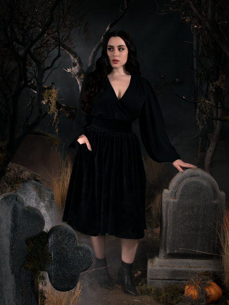 With one hand resting on the top of a tombstone and the other tucked into the pocket of her Sleepy Hollow Gothic Tales Velour Skirt in Black.