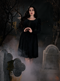 Model Rachel Sedory standing in a haunted graveyard wearing the Sleepy Hollow Gothic Tales Velour Swing Dress in Black.