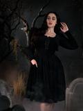 La Femme model Rachel  showing off a goth dress while posing in a haunted scene with tombstones, dead trees and fog.
