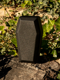 The Vamp Coffin Sunglass Case in Emerald Green standing upright on a tree stump.