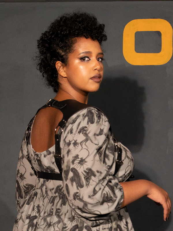 Exuding a moody, romantic allure, a female model showcases the striking silhouette of a black faux leather harness vest, blending classic gothic style clothing with a contemporary, dark-vixen aesthetic.