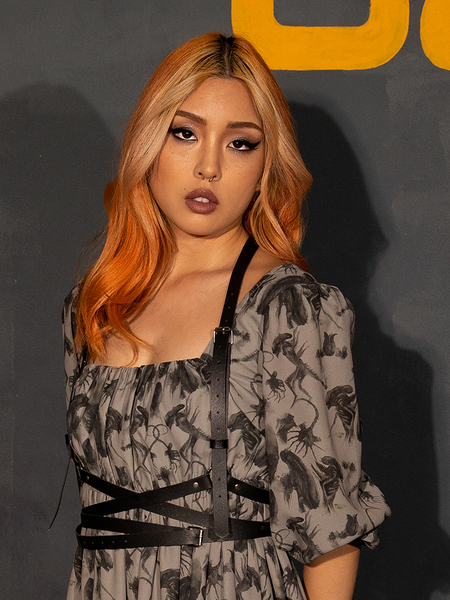 Model with orange and blonde hair looking into the camera while wearing the Body Strappy Harness in Black Faux Leather from La Femme en Noir.