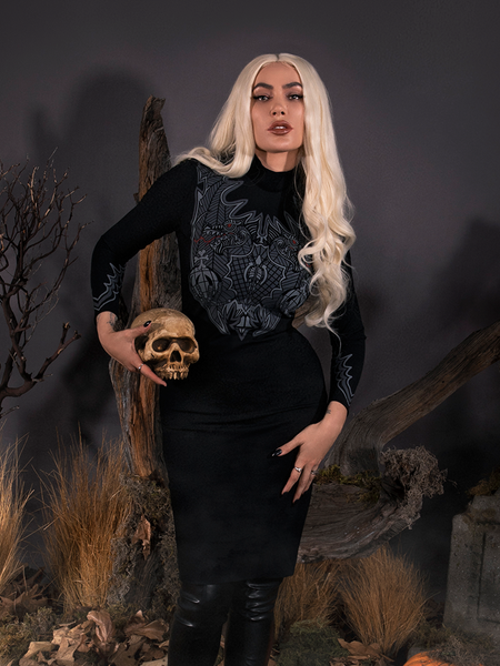 Micheline Pitt modeling the Sleepy Hollow Hessian Dress in Black while holding a weathered fake skull.